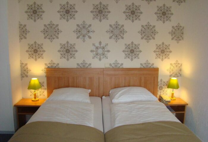 Gay-Friendly Rho Hotel room with twin beds, wooden headboard, patterned wallpaper, bedside tables, and lamps. Comfortable stay for gay travelers.