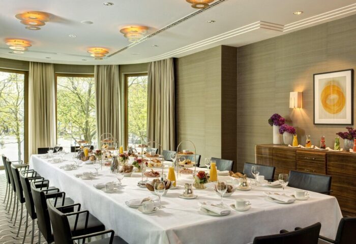 Rocco Forte The Charles Hotel: Elegant dining room setup. Long table with place settings, natural light. Gay-friendly hotel in Munich.