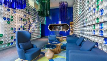 Room Mate Oscar, a gay-friendly hotel. Lobby seating area with blue sofas and chairs. Walls decorated with blue and green accents. Modern design.
