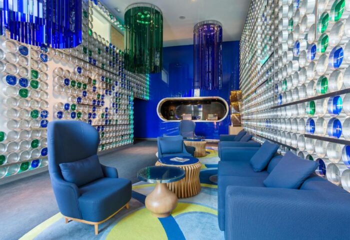 Room Mate Oscar, a gay-friendly hotel. Lobby seating area with blue sofas and chairs. Walls decorated with blue and green accents. Modern design.