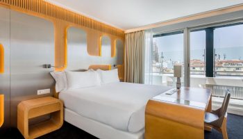 Room Mate Oscar hotel room. Gay-friendly hotel bedroom with a large bed, desk, and a view of the city. Interior design features modern, clean lines.