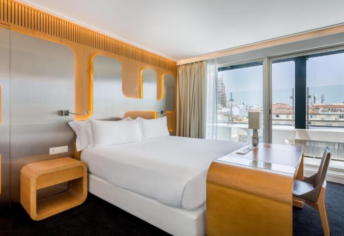 Room Mate Oscar hotel room. Gay-friendly hotel bedroom with a large bed, desk, and a view of the city. Interior design features modern, clean lines.