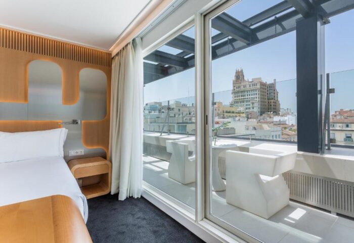Room Mate Oscar hotel room with balcony view. Gay-friendly travel lodging in Madrid. Modern design, city skyline, and bright, airy space.