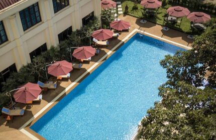 Rose Garden Hotel swimming pool aerial view. Gay-friendly hotel with umbrellas, tables, and chairs. Relaxing vacation spot.