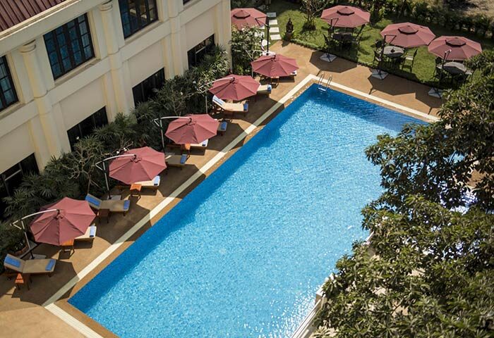 Rose Garden Hotel swimming pool aerial view. Gay-friendly hotel with umbrellas, tables, and chairs. Relaxing vacation spot.