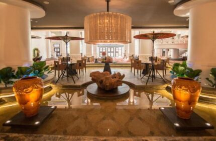 Rose Garden Hotel's lobby, a gay-friendly hotel. Water feature, tables with umbrellas, and a grand chandelier. Elegant decor.
