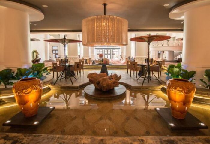 Rose Garden Hotel's lobby, a gay-friendly hotel. Water feature, tables with umbrellas, and a grand chandelier. Elegant decor.