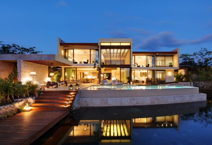 Rosewood Mayakoba gay-friendly hotel at dusk. Luxury villa with pool reflecting in water. Modern architecture, warm lighting, inviting ambiance.