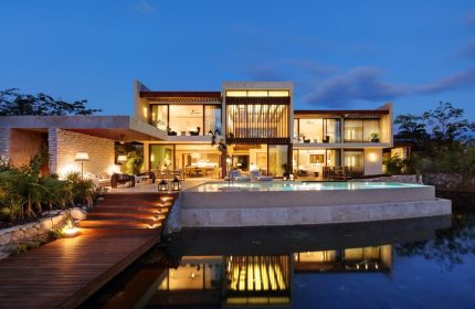 Rosewood Mayakoba gay-friendly hotel at dusk. Luxury villa with pool reflecting in water. Modern architecture, warm lighting, inviting ambiance.