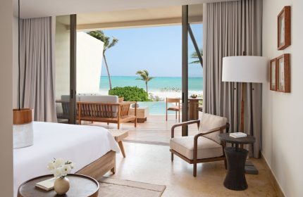 Rosewood Mayakoba gay-friendly hotel suite. Ocean view from room, with a deck, lounge seating, and palm trees. Luxury gay travel destination.