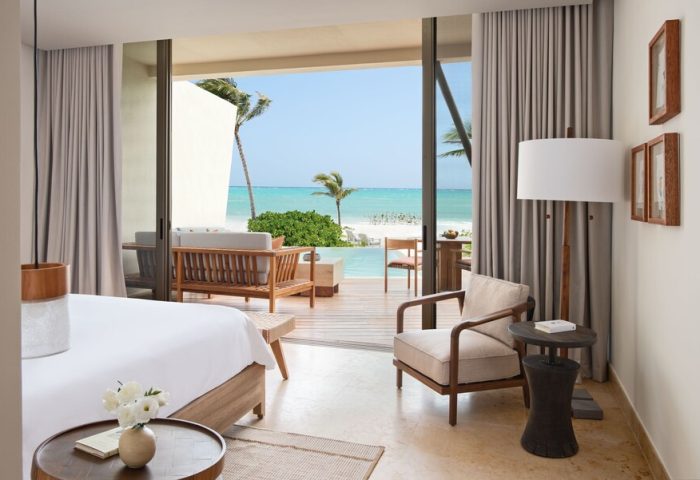 Rosewood Mayakoba gay-friendly hotel suite. Ocean view from room, with a deck, lounge seating, and palm trees. Luxury gay travel destination.