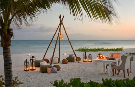 Rosewood Mayakoba gay-friendly hotel: romantic beach dinner setup with lanterns, teepee, and cushions at sunset. Ideal for LGBTQ+ travel.