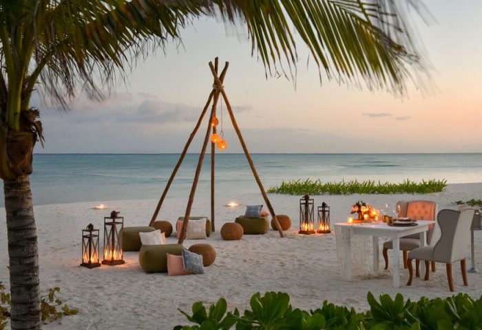 Rosewood Mayakoba gay-friendly hotel: romantic beach dinner setup with lanterns, teepee, and cushions at sunset. Ideal for LGBTQ+ travel.