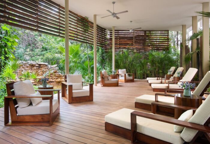 Rosewood Mayakoba gay-friendly hotel lounge area. Wooden chairs and loungers on a deck overlooking lush greenery. Relaxing, luxury travel.