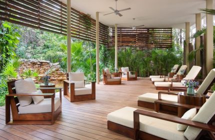 Rosewood Mayakoba gay-friendly hotel lounge area. Wooden chairs and loungers on a deck overlooking lush greenery. Relaxing, luxury travel.