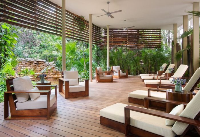 Rosewood Mayakoba gay-friendly hotel lounge area. Wooden chairs and loungers on a deck overlooking lush greenery. Relaxing, luxury travel.