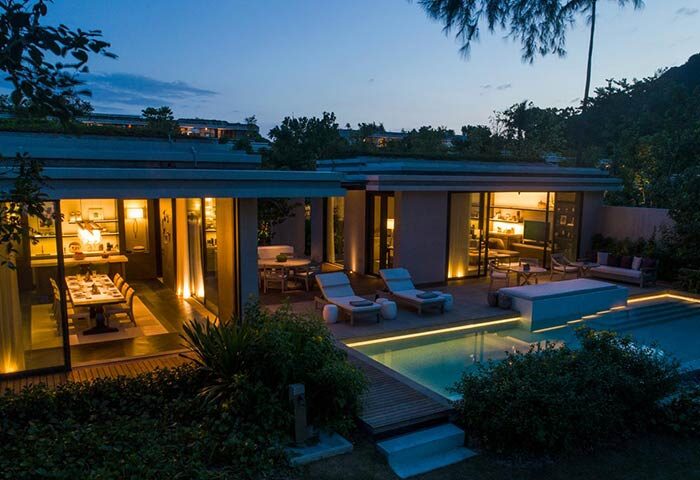 Rosewood Phuket gay-friendly hotel villa at dusk. Private pool, deck chairs, dining area. Luxury gay travel in Thailand.