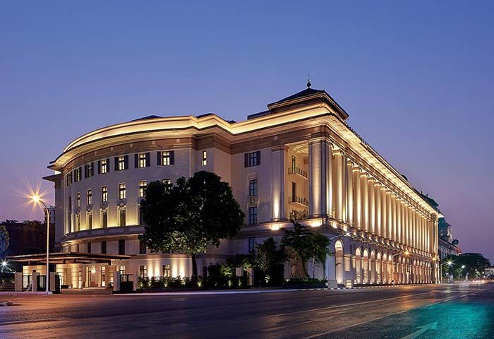 Rosewood Yangon, a gay-friendly, pet-friendly hotel. The exterior of the luxury hotel is illuminated at dusk, showcasing its grand architecture.