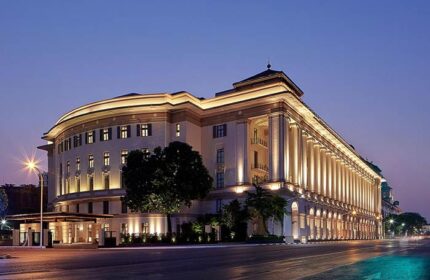 Rosewood Yangon, a gay-friendly, pet-friendly hotel. The exterior of the luxury hotel is illuminated at dusk, showcasing its grand architecture.