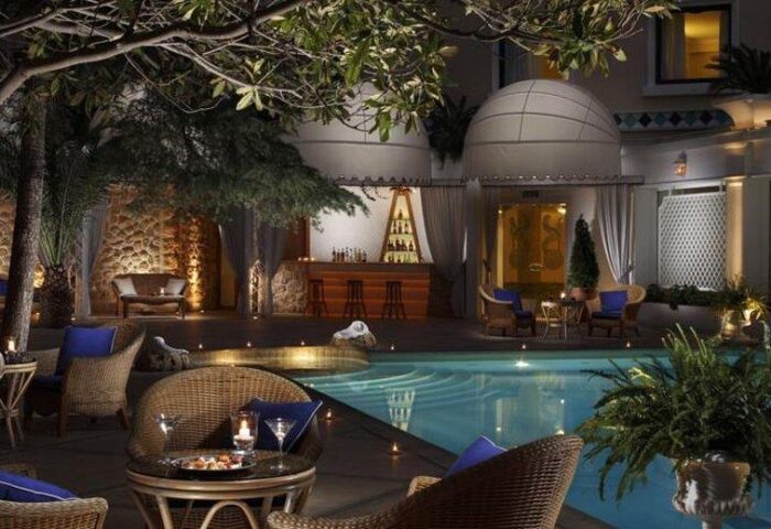 Royal Olympic Hotel gay-friendly pool area at night. Outdoor bar, lounge seating, and illuminated pool create a luxurious, inviting ambiance.