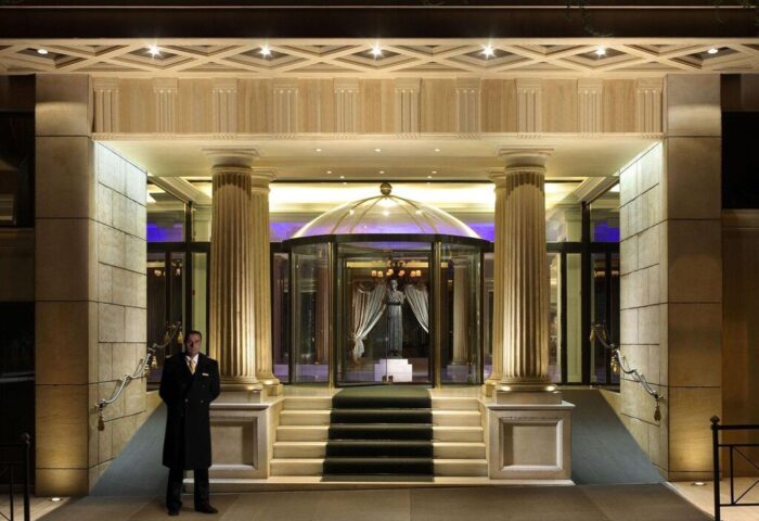 Royal Olympic Hotel entrance at night. Gay-friendly hotel with revolving doors, columns, and doorman. Luxurious travel for gay men.