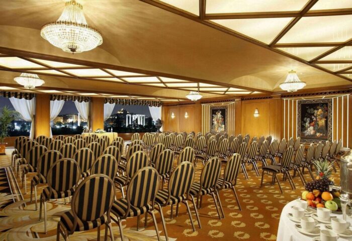 Royal Olympic Hotel ballroom setup for event. Gay-friendly hotel in Athens, Greece. Rows of chairs face a stage, with chandeliers overhead.