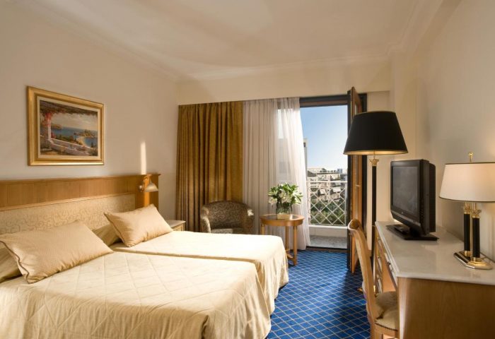Royal Olympic Hotel room. Gay-friendly hotel featuring twin beds, blue carpet, balcony, TV, desk, and city views for gay men travelers.
