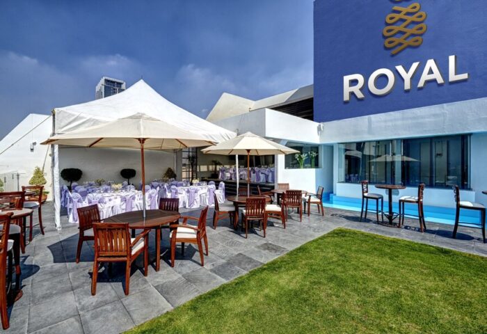 Hotel Royal Reforma's outdoor patio. Gay-friendly hotel in Zona. Tables with umbrellas and chairs, event tent, and lawn. Royal logo on the building.