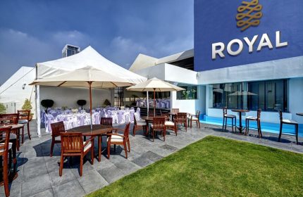 Hotel Royal Reforma's outdoor patio. Gay-friendly hotel in Zona. Tables with umbrellas and chairs, event tent, and lawn. Royal logo on the building.