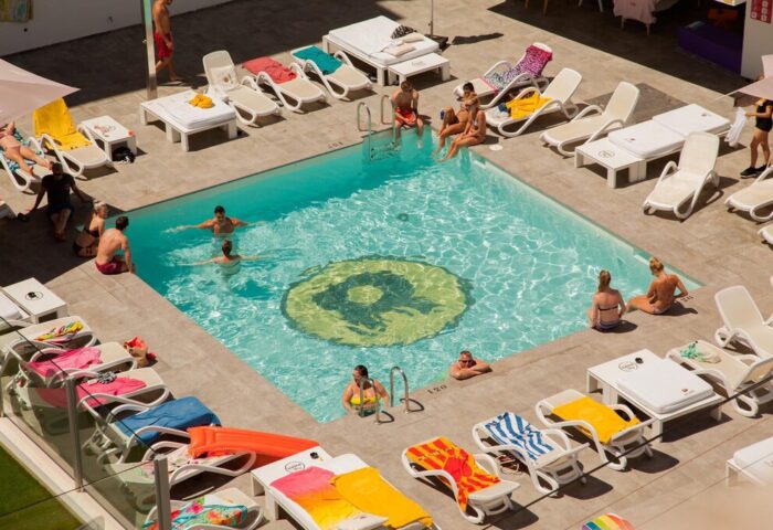 Ryans Ibiza Apartments pool aerial view. Gay-friendly, adults-only hotel with sunbeds, logo in pool. Ideal for gay travel advice.
