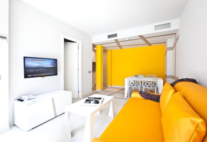 Ryans Ibiza Apartments interior. Adults only, gay-friendly hotel. Modern design with yellow accents, sofa, and dining area. Ibiza travel.