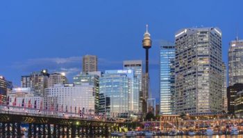 Sydney skyline at dusk. Gay-friendly Rydges World Square hotel in view. Gay travel advice for lodging near harbor.