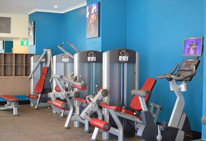 Rydges World Square gay-friendly hotel gym. Exercise machines with red cushions against a blue wall. Fitness center at this Sydney hotel.