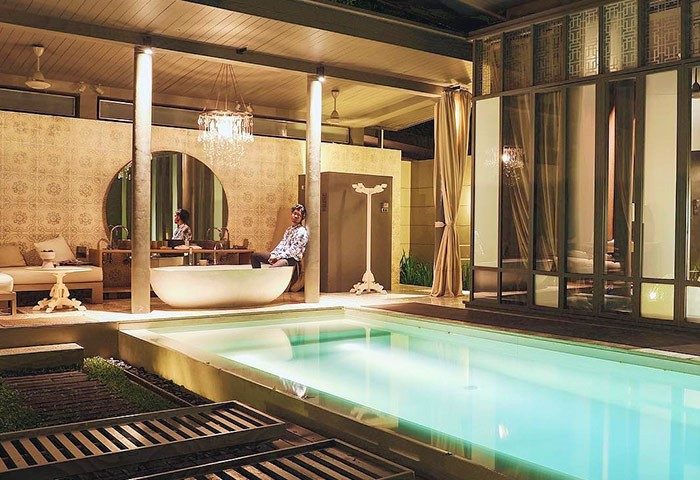 Gay-friendly SALA Phuket Mai Khao Beach Resort suite. Man relaxing by the pool, luxurious bathroom with tub. Ideal for gay travel.