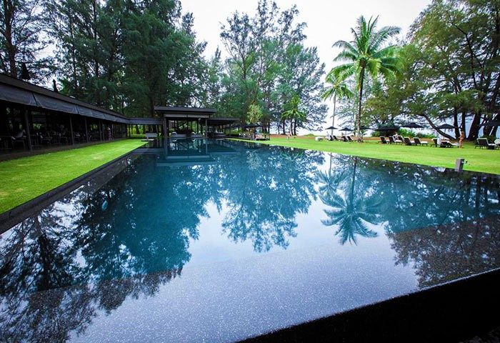 SALA Phuket Mai Khao Beach Resort pool. Gay-friendly hotel with palm trees reflecting in the water. Perfect for gay travel.