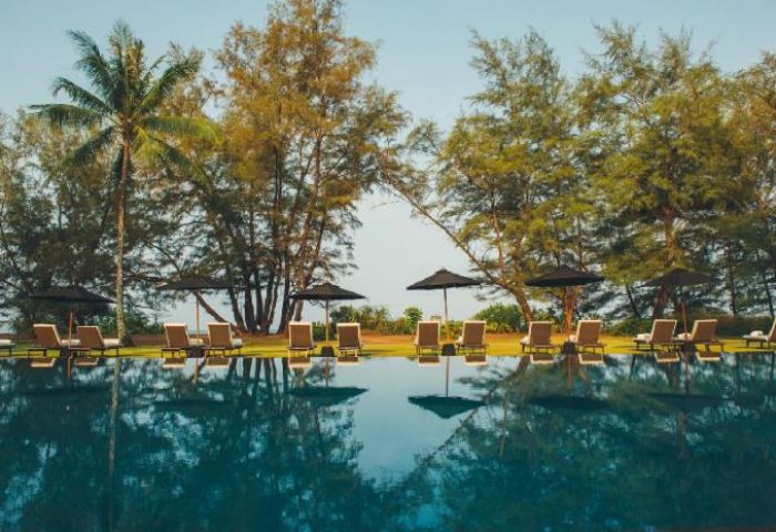 SALA Phuket Mai Khao Beach Resort pool view. Gay-friendly hotel with palm trees, lounge chairs, and umbrellas. Serene Mai Khao beach resort.