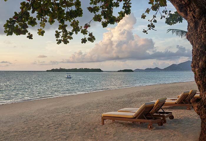 Beachfront view at SALA Samui Chaweng Beach, a gay-friendly hotel. Lounge chairs on the sand, tranquil sea, and scenic islands. Perfect for gay travel.