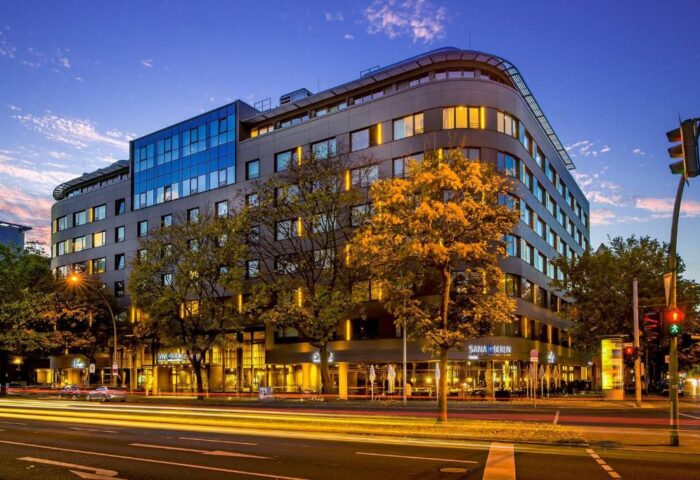 SANA Berlin Hotel exterior at dusk. Gay-friendly, pet-friendly hotel with modern architecture. Street view with light trails. Berlin travel.