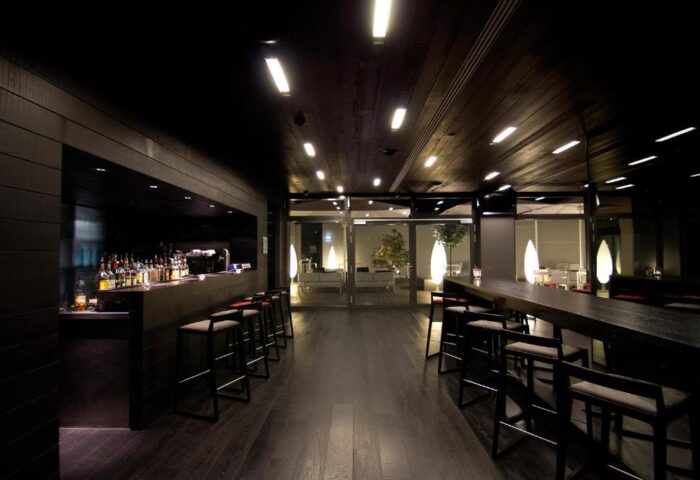 SANA Berlin Hotel bar interior. Gay-friendly, pet-friendly hotel with dark wood decor, bar stools, and a view to an outdoor seating area.