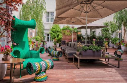 SO/ Berlin Das Stue gay-friendly hotel's pet-friendly outdoor lounge area with unique green furniture and umbrellas. Stylish and inviting.