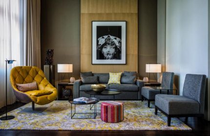 SO/ Berlin Das Stue hotel interior. Gay-friendly, pet-friendly hotel room with yellow chair, grey sofa, and modern art. Stylish Berlin stay.