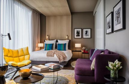 SO/ Berlin Das Stue gay-friendly hotel room. Pet-friendly hotel with yellow chair, purple sofa, bed, and modern decor. Stylish, comfortable.