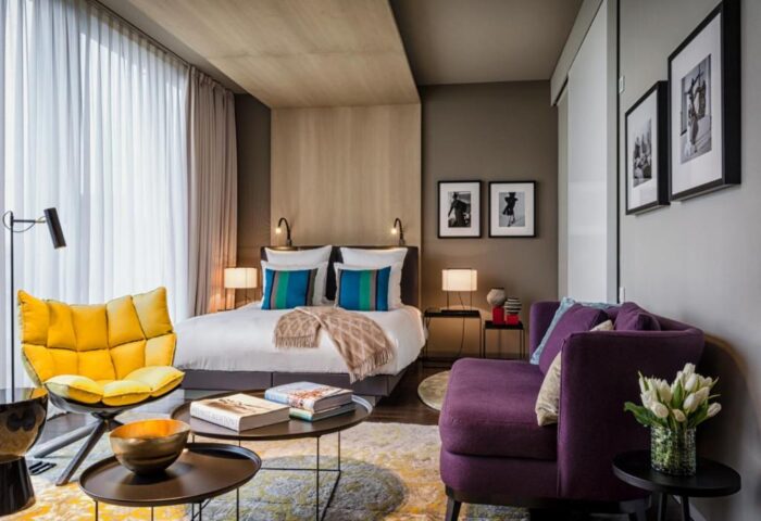 SO/ Berlin Das Stue gay-friendly hotel room. Pet-friendly hotel with yellow chair, purple sofa, bed, and modern decor. Stylish, comfortable.