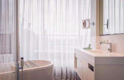 SO/ Berlin Das Stue bathroom. Gay-friendly, pet-friendly hotel with bathtub, sink, mirror, and sheer curtains. Modern design.