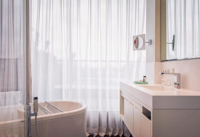 SO/ Berlin Das Stue bathroom. Gay-friendly, pet-friendly hotel with bathtub, sink, mirror, and sheer curtains. Modern design.