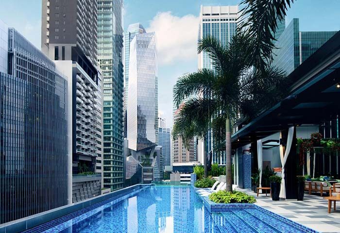 Rooftop pool at SO/ Sofitel Singapore, a gay-friendly hotel. City skyline view, palm trees, and lounge area. Ideal for LGBT travelers.