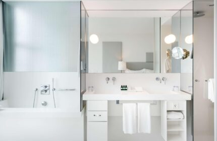 SO/ Vienna gay-friendly hotel bathroom. Modern, all-white decor with bathtub, double sinks, and glass shower. Upscale travel for gay men.