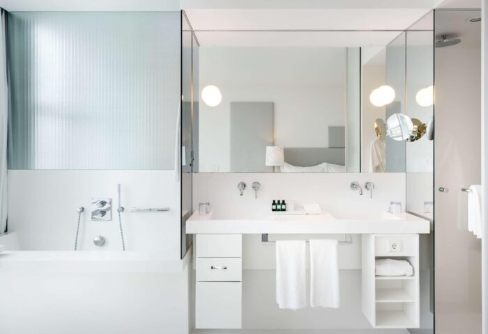 SO/ Vienna gay-friendly hotel bathroom. Modern, all-white decor with bathtub, double sinks, and glass shower. Upscale travel for gay men.