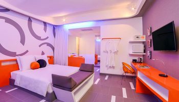 SUN & MOON Urban Hotel, gay-friendly room. Modern design with bed, orange accents, desk, and TV. Ideal for gay men travel, urban stay.