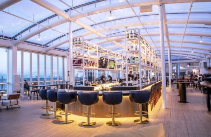 Interior of Sable at Navy Pier Chicago, a gay-friendly Curio Collection by Hilton hotel. Bar with stools, bottles, and a transparent roof.